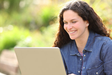 Happy woman using laptop sitting in a parkの写真素材