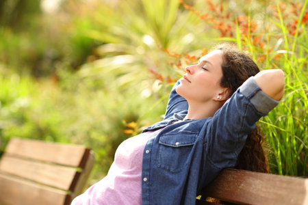 Profile of a woman relaxing and resting sitting in a bench in a parkの写真素材
