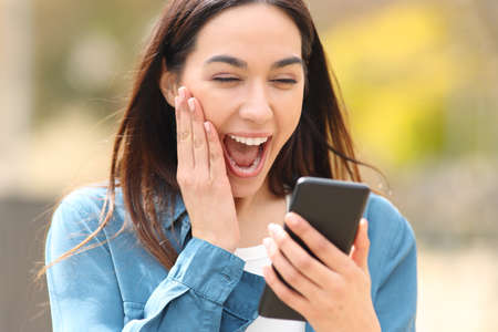 Shocked woman checking smart phone discovering surprising content outside in a parkの写真素材