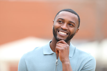 Front view portrait of a happy man with black skin thinking looking at side in the streetの写真素材