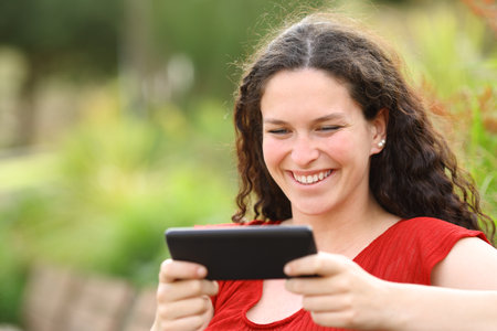 Happy woman in a park watching videos on horizontal smart phone in a parkの写真素材