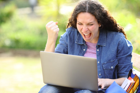 Excited woman checking laptop content sitting in a parkの写真素材