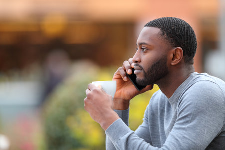 Profile portrait of a man with black skin talking on phone drinking in a coffee shopの写真素材