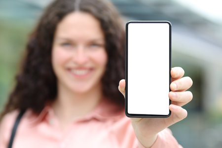 Front view portrait of a happy elegant woman showing blank phone screen in the streetの写真素材