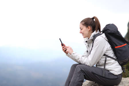 Profile of a happy mountaineer checking smart phone in the mountainの写真素材