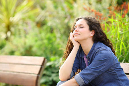 Happy woman resting with closed eyes sitting in a parkの写真素材