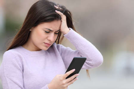 Worried teen checking bad news on smart phone in the streetの写真素材