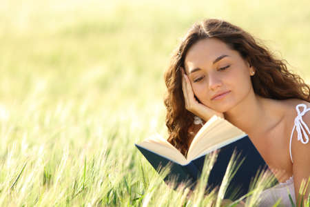 Woman reading a paper book sitting in a wheat fieldの写真素材