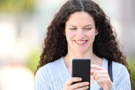 Front view portrait of a woman using phone walking in the streetの写真素材