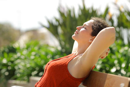 Profile of a woman resting with arms on head sitting on bench in a parkの写真素材