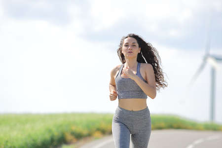 Front view portrait of a runner woman running in a road in a mill farmの写真素材