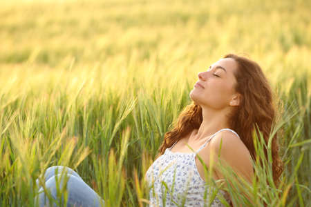 Beautiful woman relaxing breathing fresh air sitting in a wheat field at sunsetの写真素材