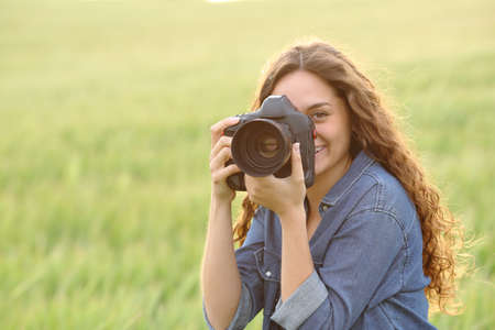 Happy woman taking photos with dslr camera looking at you in a wheat fieldの写真素材