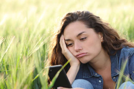 Bored woman checking smart phone sitting in a wheat fieldの写真素材