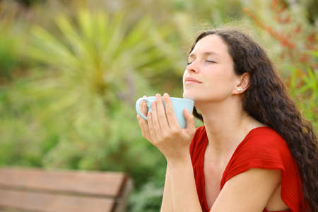 Relaxed woman smelling coffee in a green parkの写真素材
