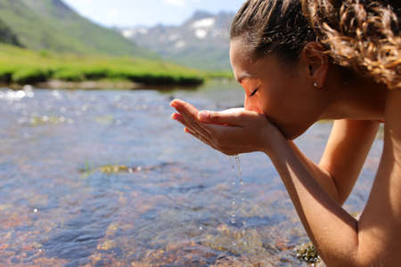 Side view portrait of a woman drinking raw water from riverの写真素材