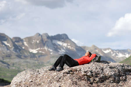 Tired hiker in red resting lying and relaxing on the top of a high mountainの写真素材