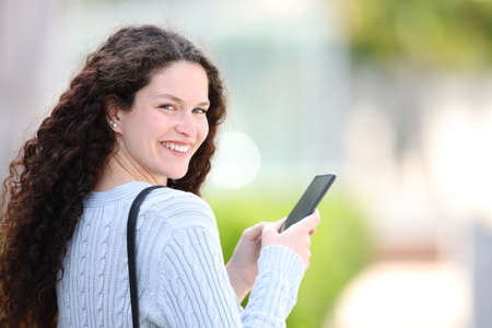 Happy woman using smart phone walking in the street twirling looking at youの写真素材