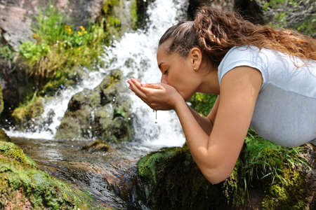 Woman drinking water from river with cupped hands in the mountainの写真素材