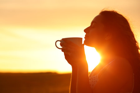 Back light silhouette of a woman smelling coffee at sunsetの写真素材