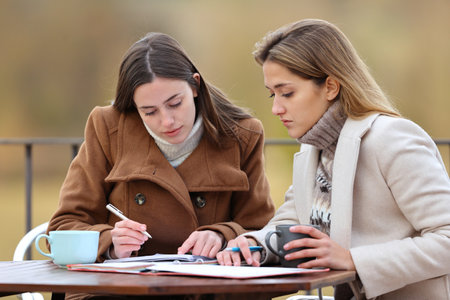 Two students checking paper notes in a terrace in winterの写真素材