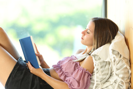 Profile of a woman reading a book lying beside a windowの写真素材
