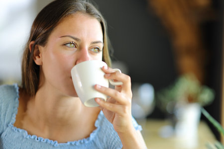 Happy woman distracted drinking coffee at homeの写真素材