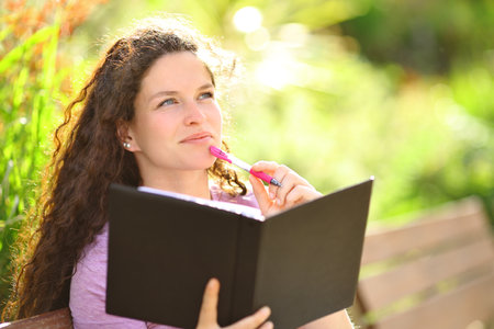 Happy woman writing on notebook and thinking in a parkの写真素材