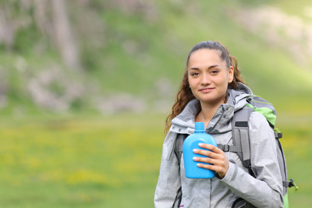 Satisfied hiker holding canteen looking at camera in the mountainの写真素材