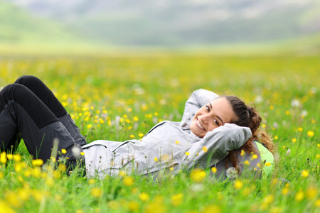 Happy hiker resting lying on the grass looks at you in the mountainの写真素材