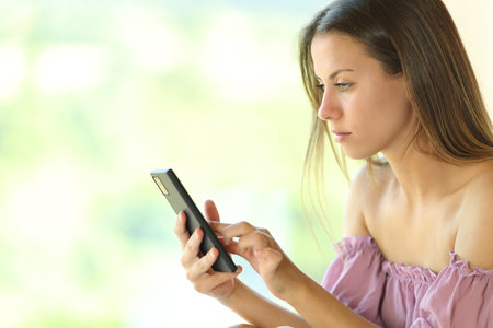 Young serious woman using smart phone near a window at homeの写真素材