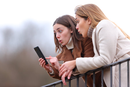 Surprised women checking smart phone from a balcony in winterの写真素材