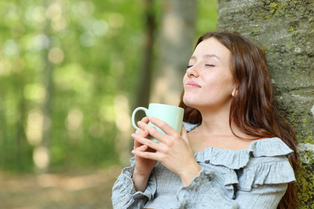 Happy woman relaxing drinking coffee sitting in a forestの写真素材
