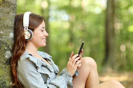 Profile of a happy woman listening to music with headphones and smartphone relaxing in a forestの写真素材