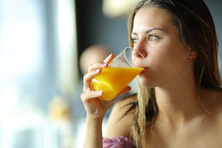 Young woman drinking orange juice looking through a windowの写真素材