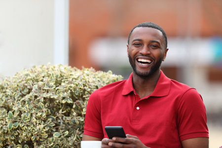 Happy black man holding mobile phone looking at you in a coffee shopの写真素材