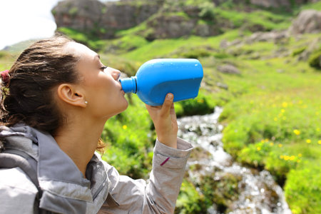 Trekker drinking water from canteen beside a creek in the mountainの写真素材