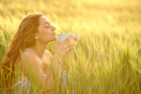 Profile of a relaxed woman drinking and smelling coffee in a wheat fieldの写真素材