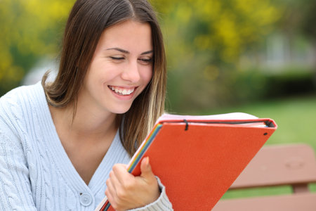 Happy student reading notes sitting on a bench in a parkの写真素材