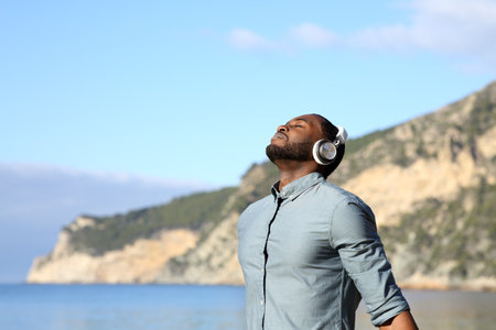 Relaxed black man meditating with wireless headphones listening to a guide on the beachの写真素材