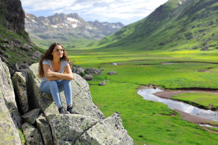 Happy woman contemplating beautiful mountain views sitting on a cliffの写真素材