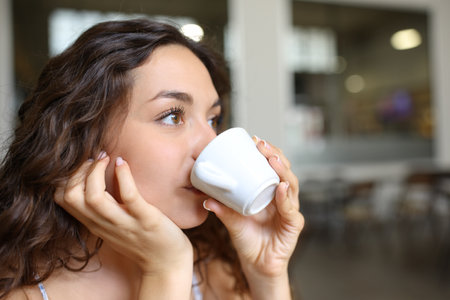 Woman drinking coffee in a bar looking awayの写真素材
