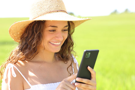 Happy woman using phone in a field on summer wearing pamela hatの写真素材