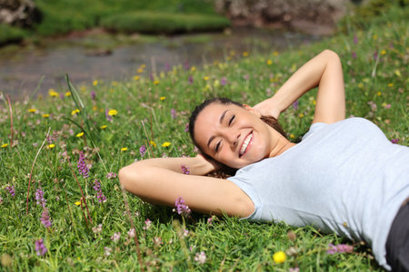 Relaxed woman lying on the grass in a riverside looking at youの写真素材