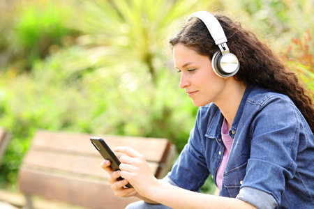 Woman listening to music with headphones and smart phone in a green parkの写真素材