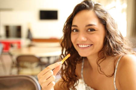 Happy woman in a coffee shop eating potato and looking at cameraの写真素材
