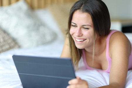 Happy teen using tablet in bed laughing at homeの写真素材