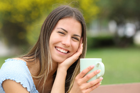 Candid happy teen looks at you holding coffee mug in a parkの写真素材