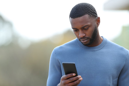Sad black man reading chat on phone in the streetの写真素材