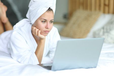 Woman in the bed after showering using laptop on a bedの写真素材